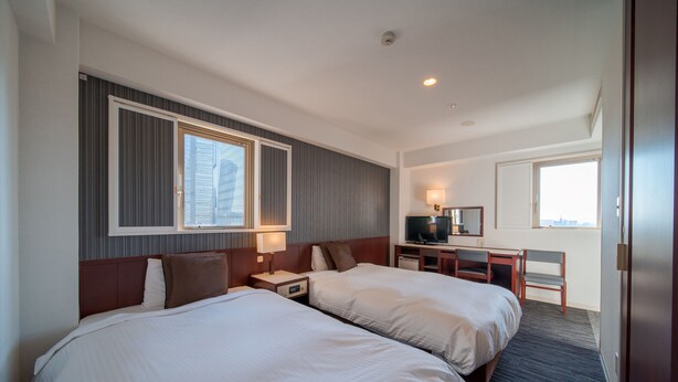 A hotel room with two beds, a desk, a TV, and a window with a city view.
