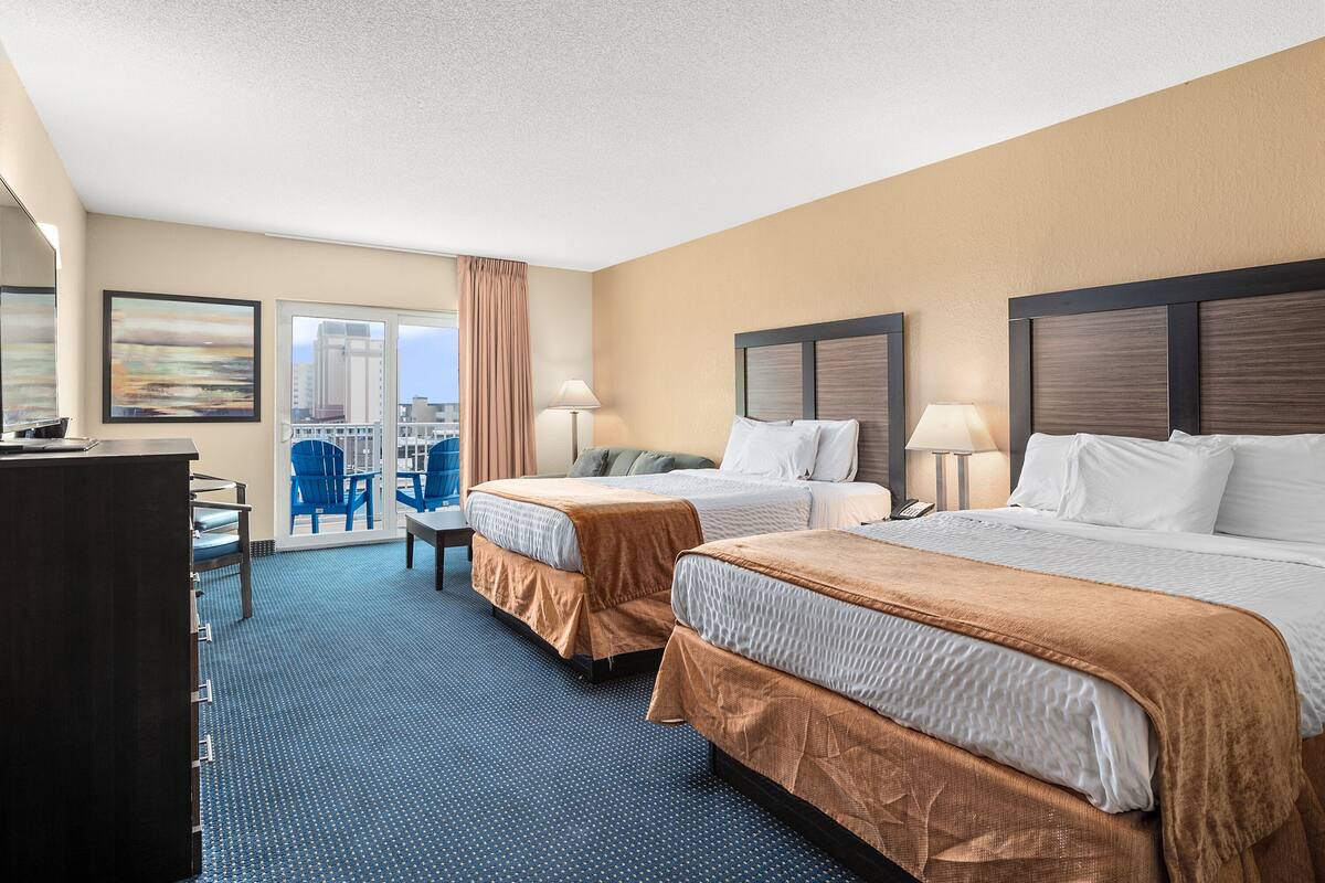 A hotel room with two beds, a desk, chairs, and a view of the city.