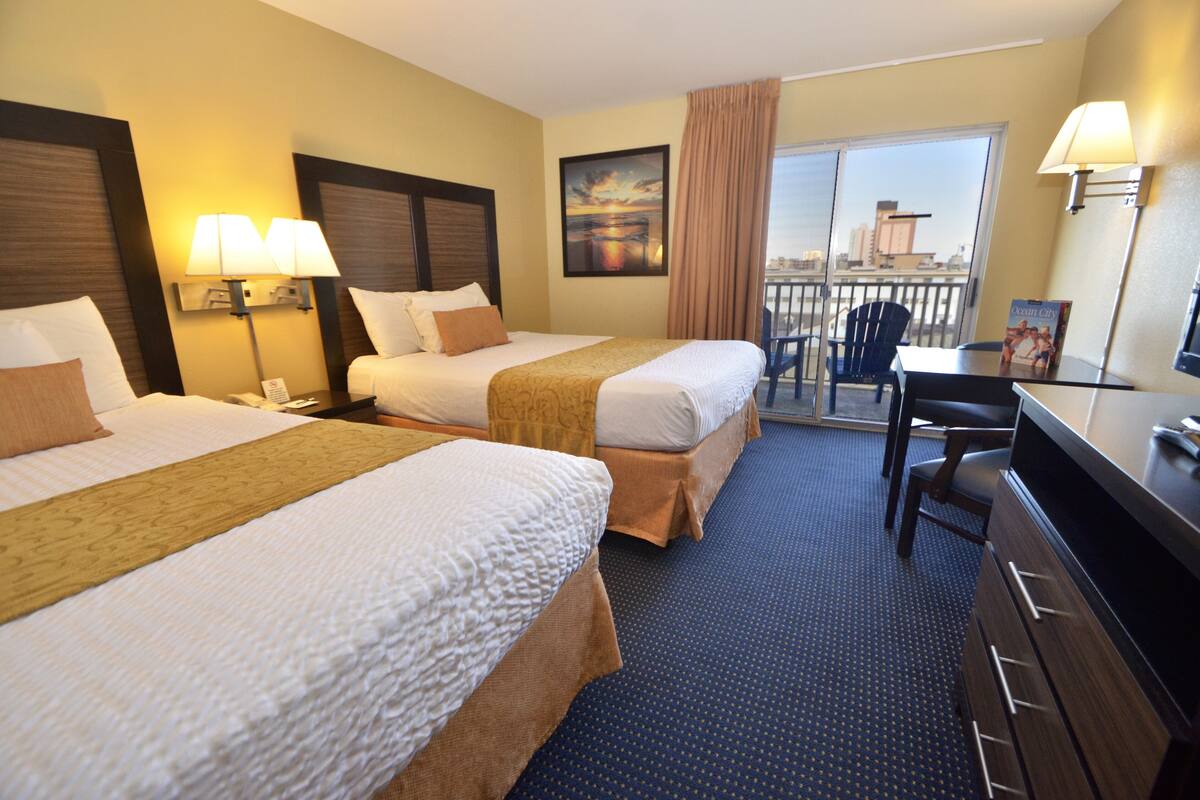 A hotel room with two beds, a desk, a chair, a TV, and a balcony with a city view.