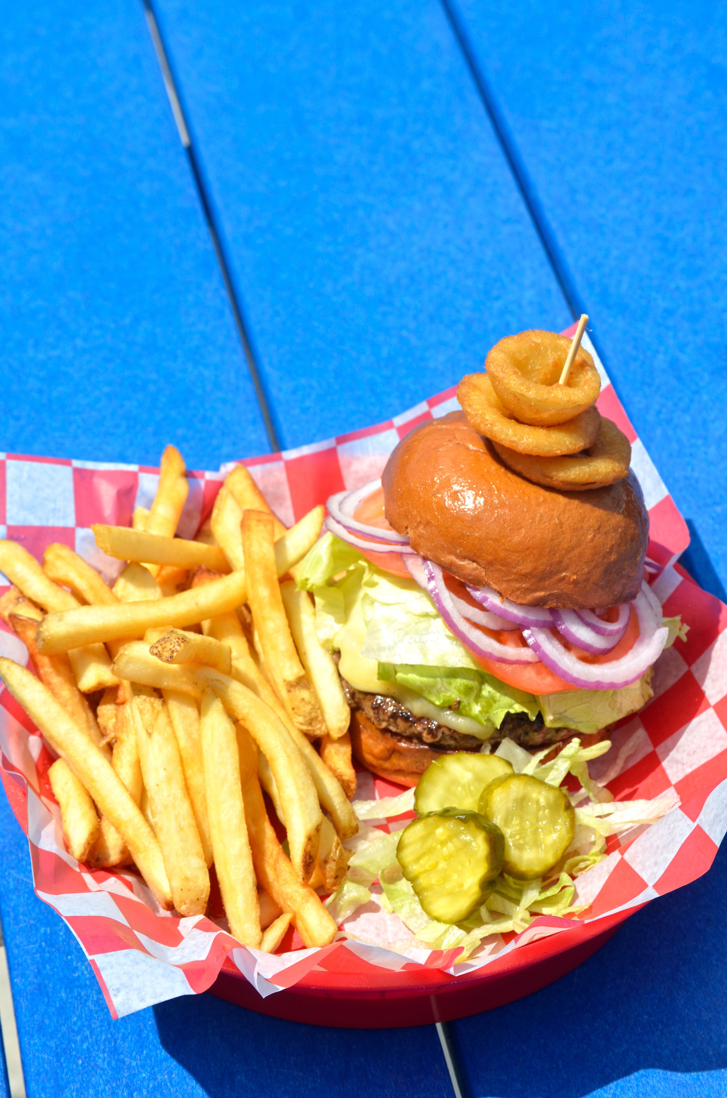 A burger with fries and pickles on a red and white checkered paper.