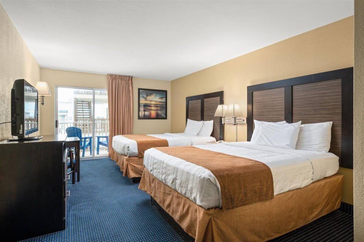 A hotel room with two beds, a desk, a chair, and a balcony with a view.