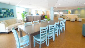 Uma ampla sala de jantar com uma mesa comprida e várias cadeiras, um balcão de recepção e uma área de estar com sofá e poltronas.
