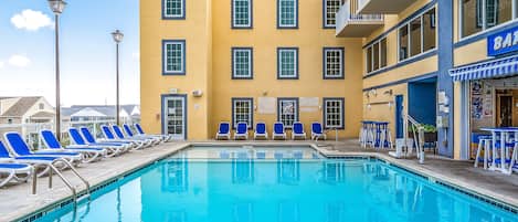 A pool area with blue lounge chairs and a building with multiple windows and balconies.