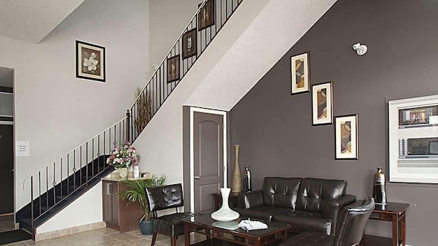 Een woonkamer met een donkerbruine leren bank, een bijzettafeltje en een trap met een zwarte balustrade.