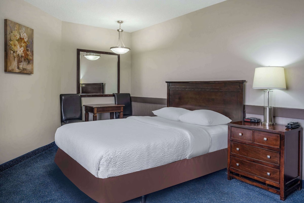 Habitación de hotel con una cama grande, un escritorio, una silla, un aparador, un espejo y una lámpara.