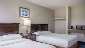 Hotelkamer met twee bedden, een nachtkastje met een lamp, een magnetron en een inlijsting foto aan de muur.