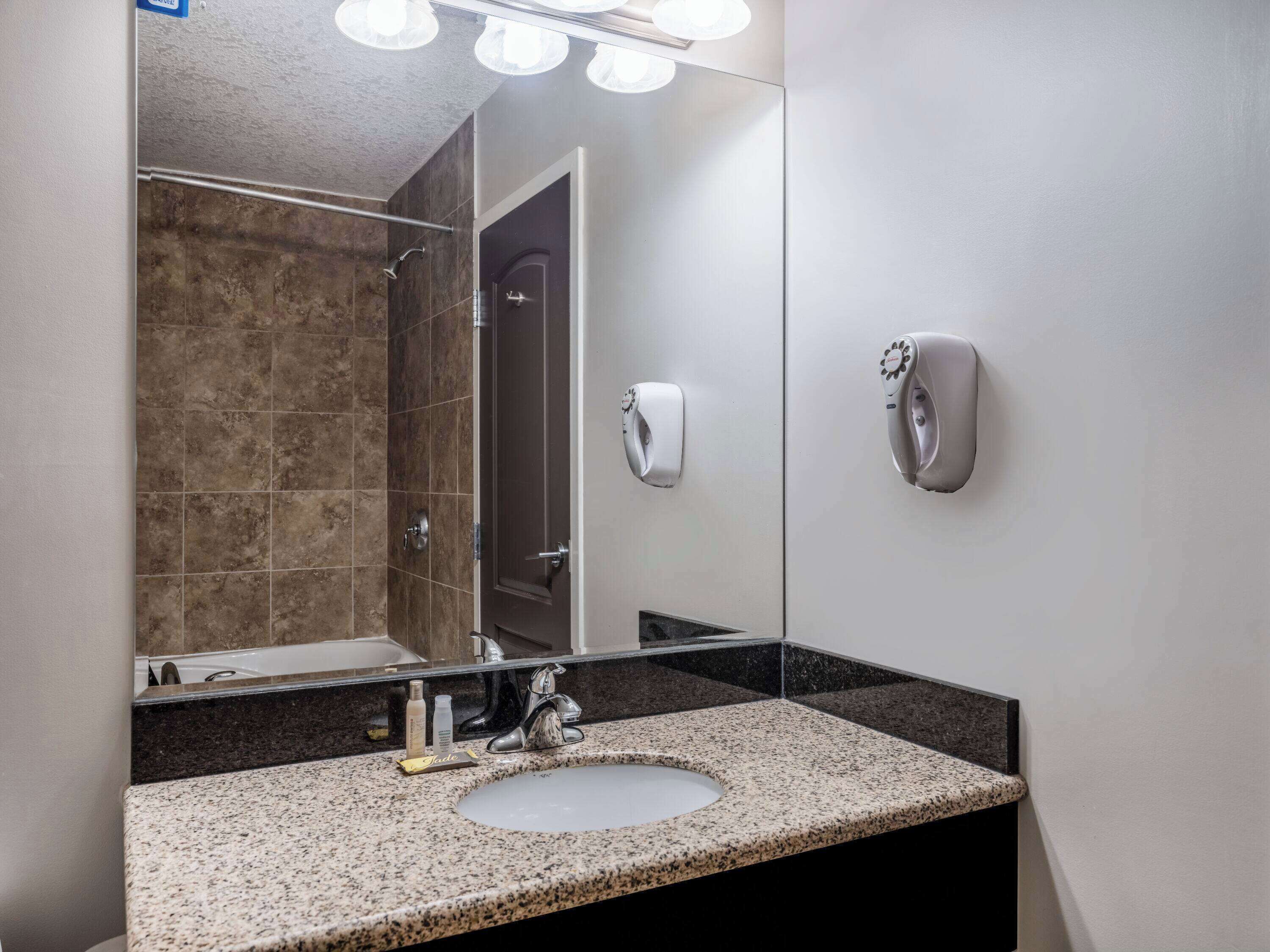 Un bagno moderno con un piano in granito, un lavandino, uno specchio e un dispenser di sapone a portata di mano.