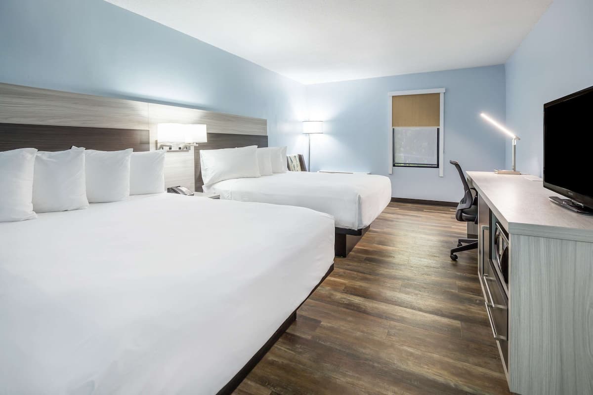 A hotel room with two beds, a desk with a TV, a lamp, and a window with blinds.