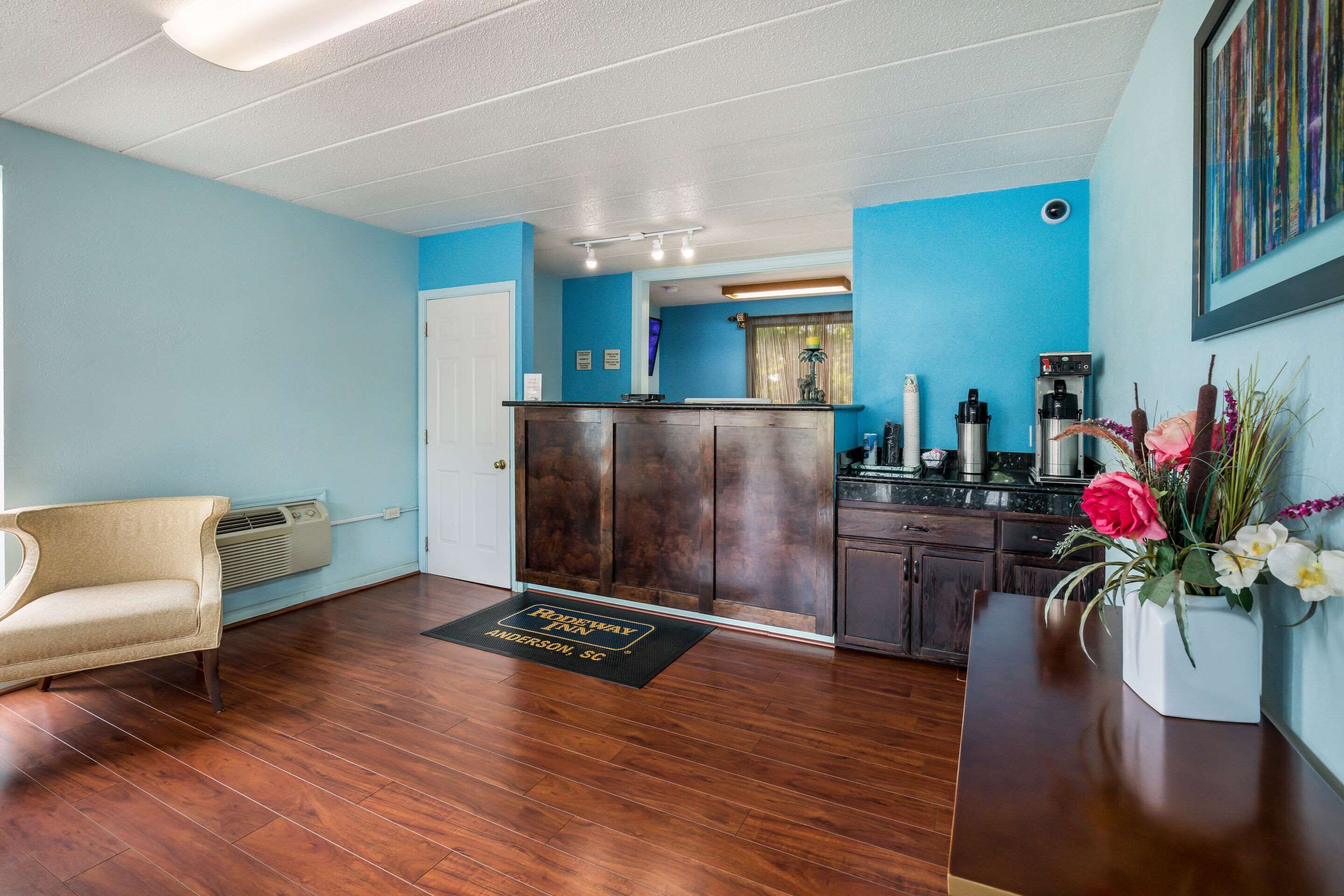 A hotel lobby with a wooden reception desk, a beige sofa, a kitchen area, and a blue wall.