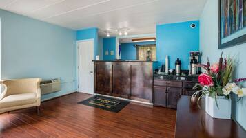A hotel lobby with a wooden reception desk, a beige sofa, a kitchen area, and a blue wall.