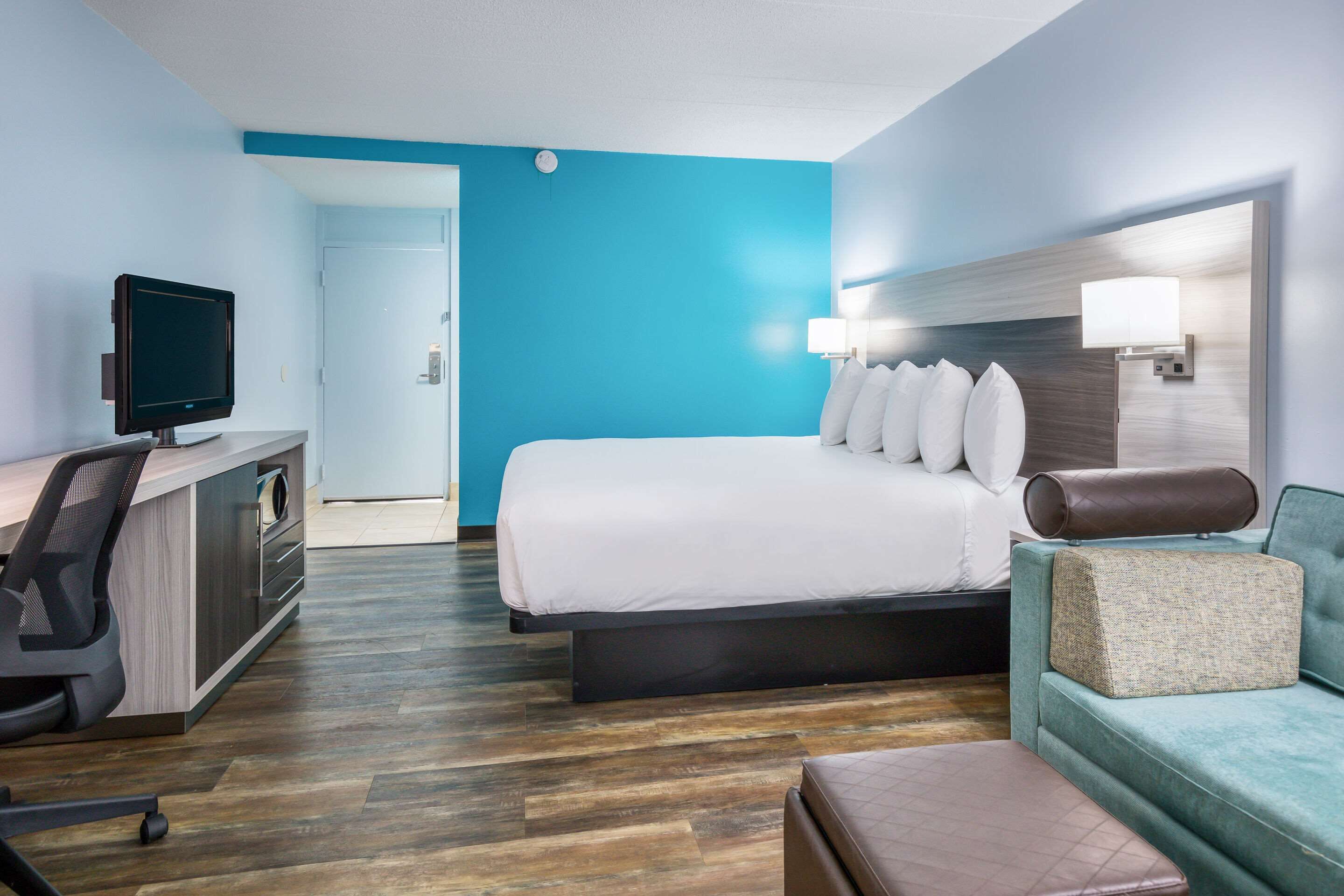 Quarto de hotel com cama, escrivaninha com computador, sofá e televisão.