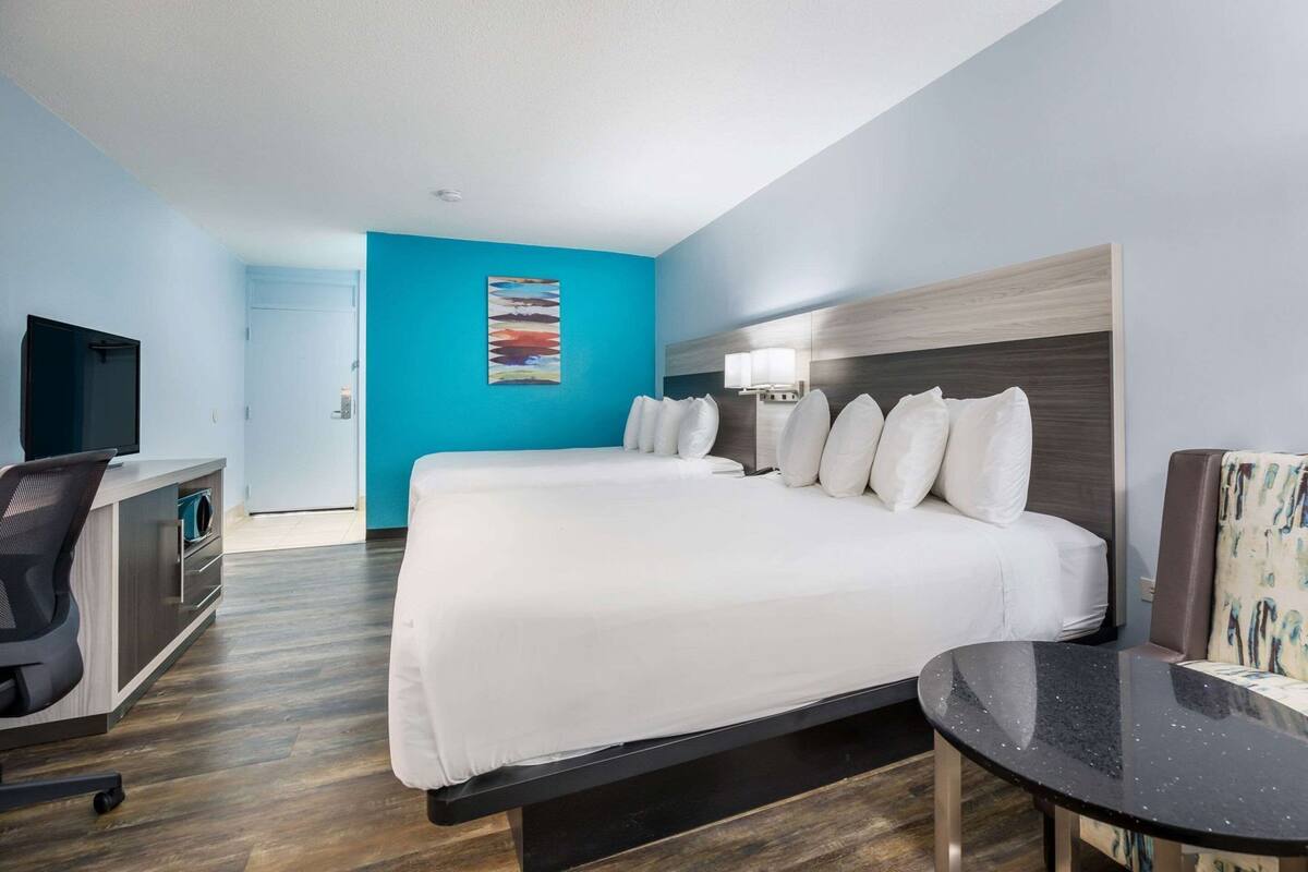 A hotel room with a large bed, a desk with a chair, a television, and a painting on the wall.