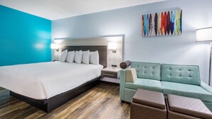 A hotel room with a large bed, a sofa, and a small table. - Rodeway Inn Anderson North - Clemson (Anderson)
