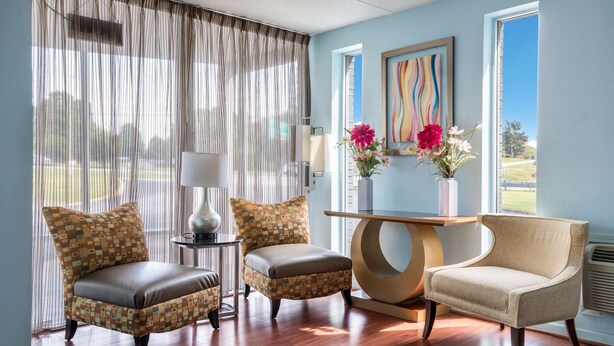 A room with a wooden floor, two patterned armchairs, a small table, and a vase with flowers. - Rodeway Inn Anderson North - Clemson (Anderson)
