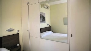 Habitación de hotel con un espejo grande, una cama, una mesita de noche con teléfono y aire acondicionado de pared.