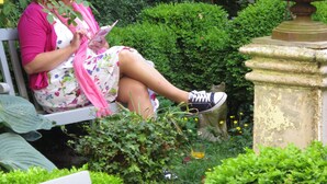 Una mujer sentada en un banco en un jardín, con una mesa y sillas cerca.