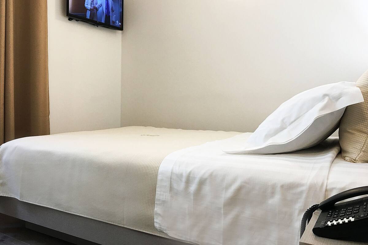 Habitación de hotel con una cama individual, un televisor montado en la pared y un teléfono en la mesita de noche.