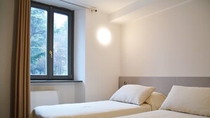 Una habitación con dos camas, una ventana con cortinas y una lámpara fijada a la pared.