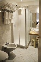 Un baño moderno con ducha envuelta en vidrio, un bidé, un inodoro y un lavabo con espejo.