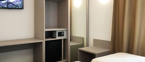 Una habitación de hotel con cama, escritorio, televisor y minibar.