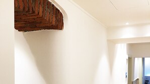 Un pasillo con una pared blanca curva, un detalle de pared de ladrillo y un suelo de madera con una franja negra.