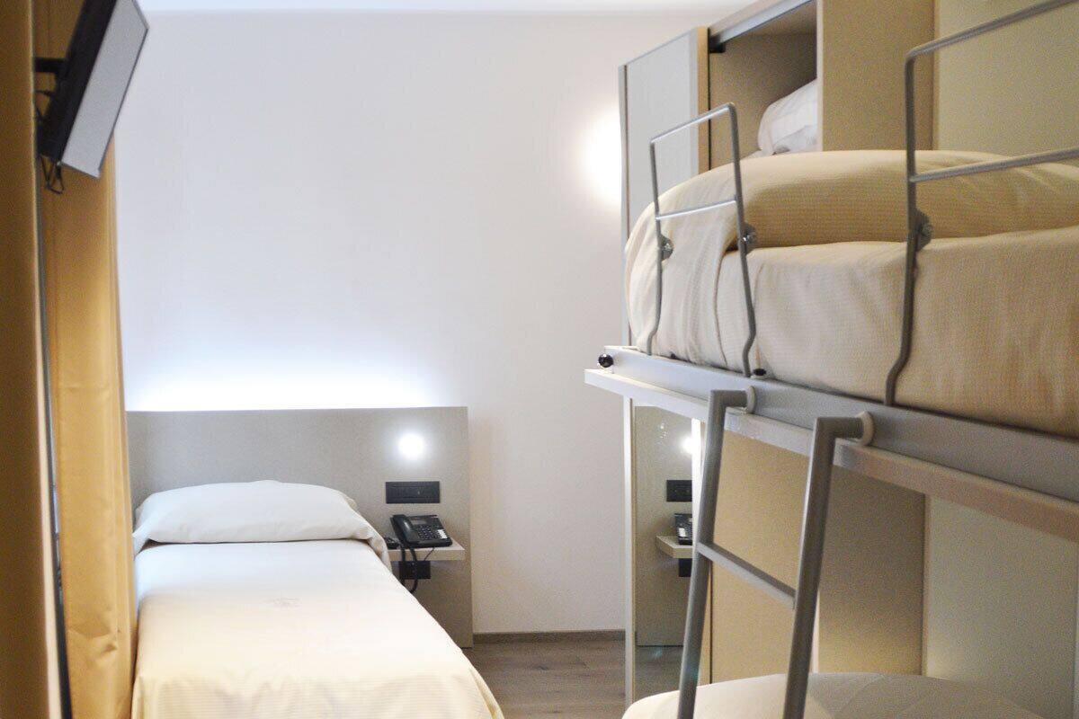 Habitación de hotel con literas, una mesita de noche con lámpara y un televisor montado en la pared.