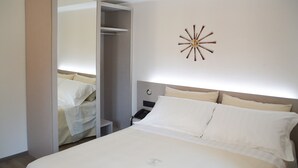 Una habitación de hotel con cama, mesita de noche, espejo y un reloj de pared.