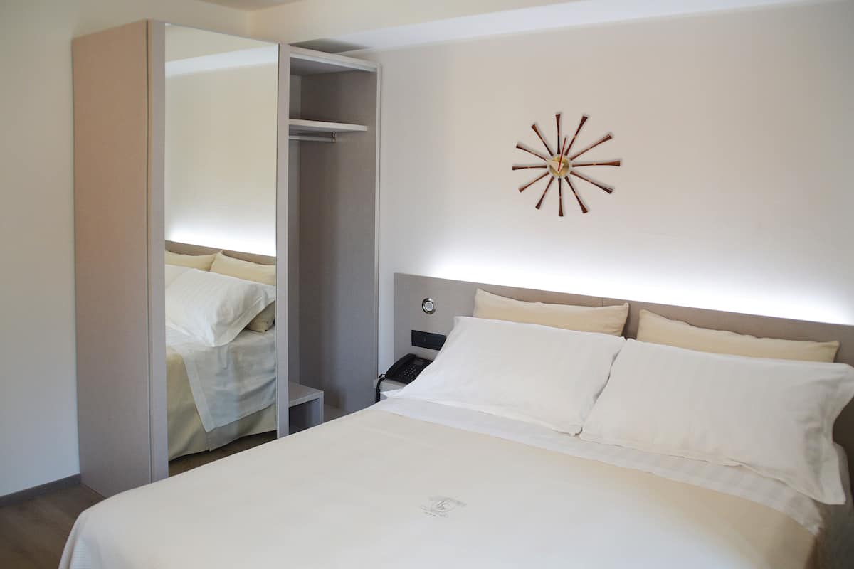 Una habitación de hotel con cama, mesita de noche, espejo y un reloj de pared.