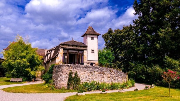 A stone building with a tower, surrounded by a well-maintained garden and a gravel path. - Domaine de Borie Chambres d'Hôtes (Bretenoux)