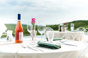 Mesa lista para cenar al aire libre con una botella de vino, una rosa y copas de cristal.