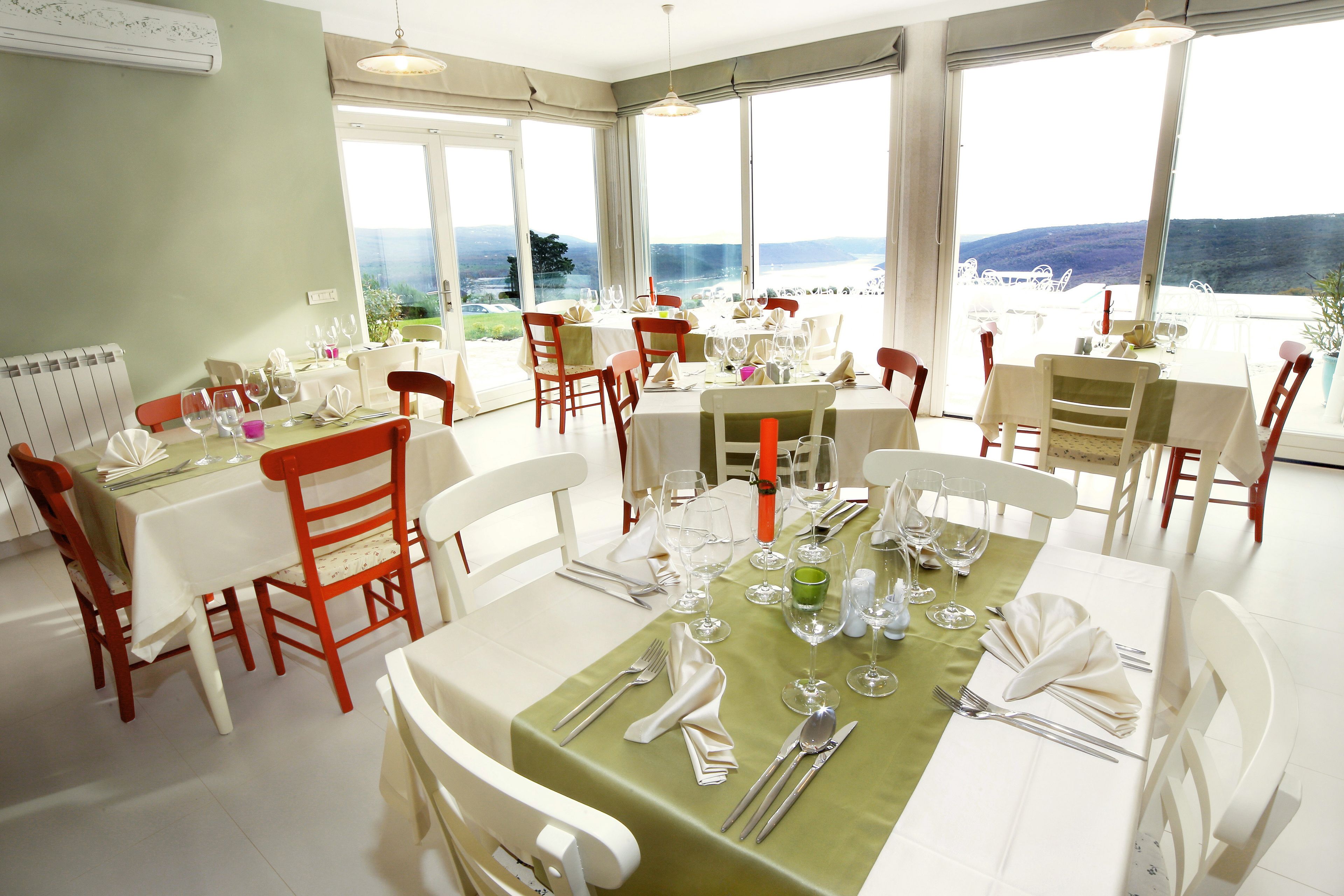 A dining area with tables set for a meal, large windows offering a view of the landscape, and a radiator on the wall.
