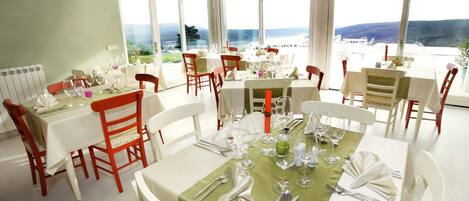 A dining area with tables set for a meal, large windows offering a view of the landscape, and a radiator on the wall.