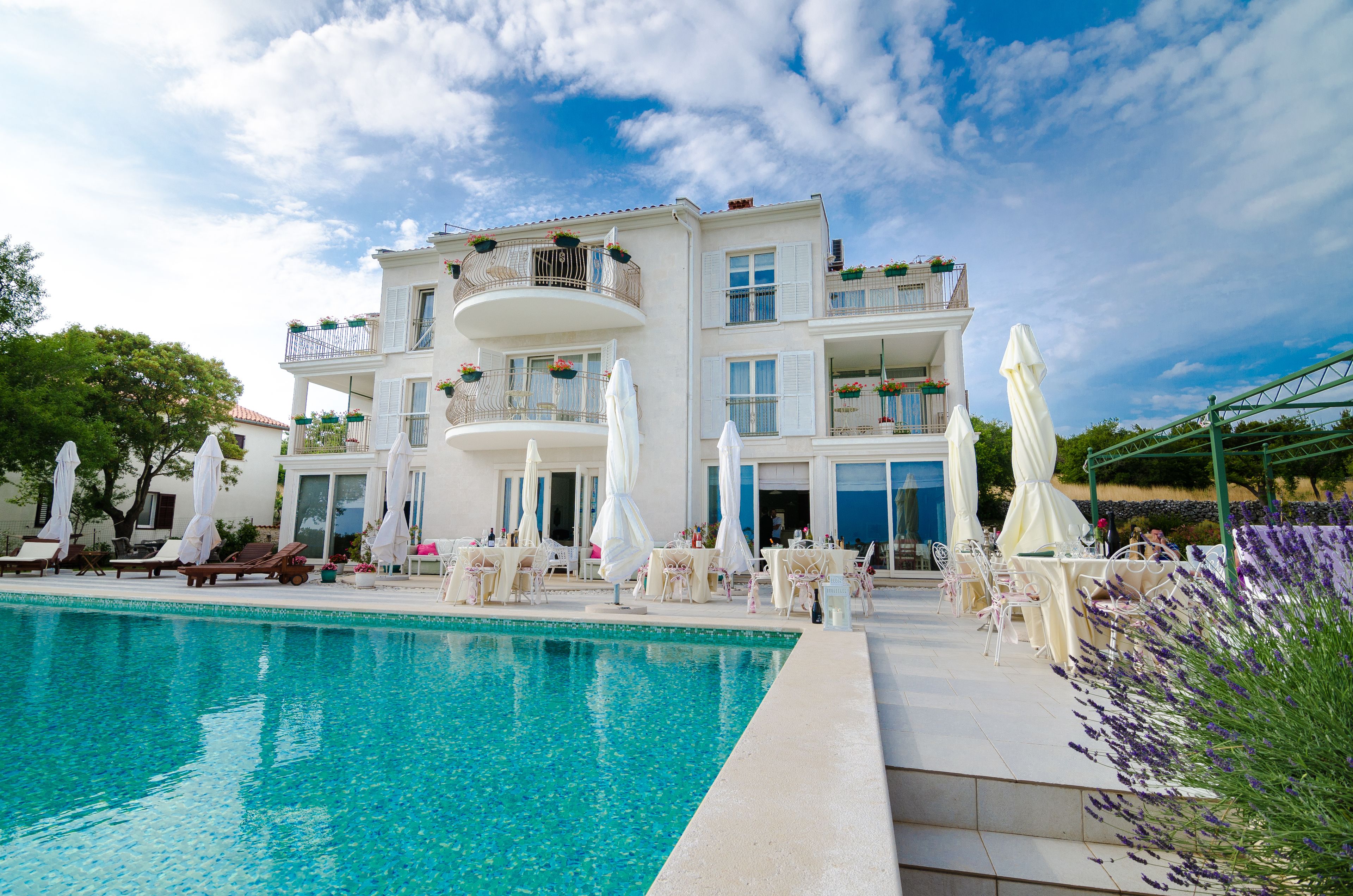 Un hotel con piscina, mobiliario exterior y balcones con plantas.