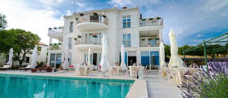 Un hotel con piscina, mobiliario exterior y balcones con plantas.