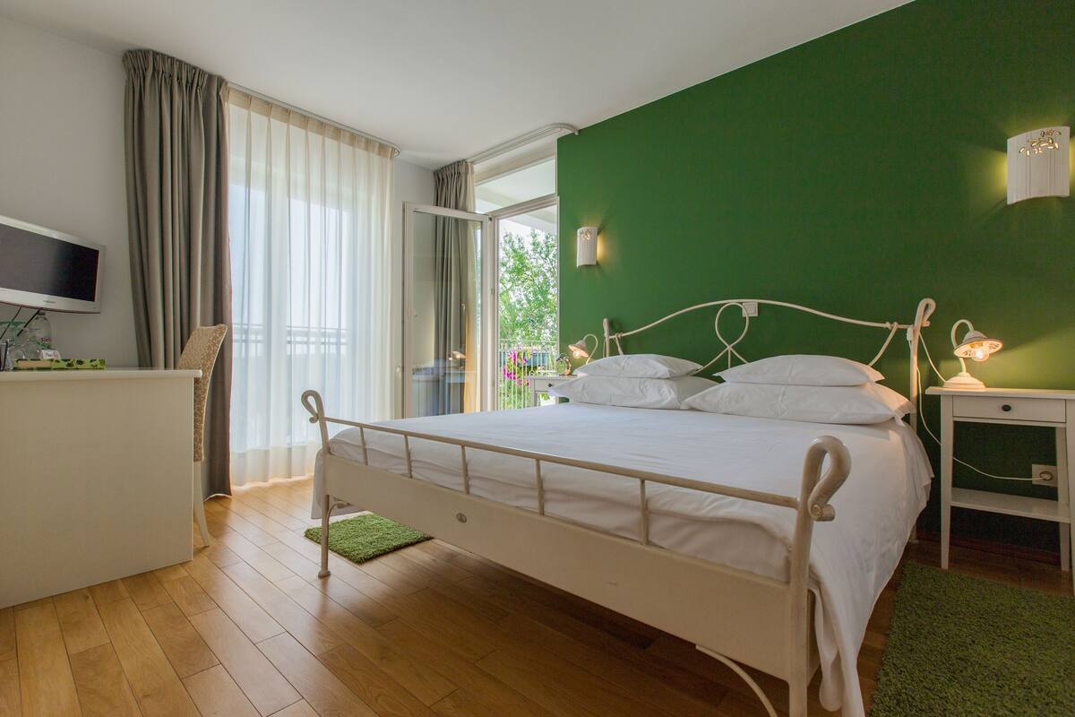 A bedroom with a bed, a desk, a TV, and a green wall.