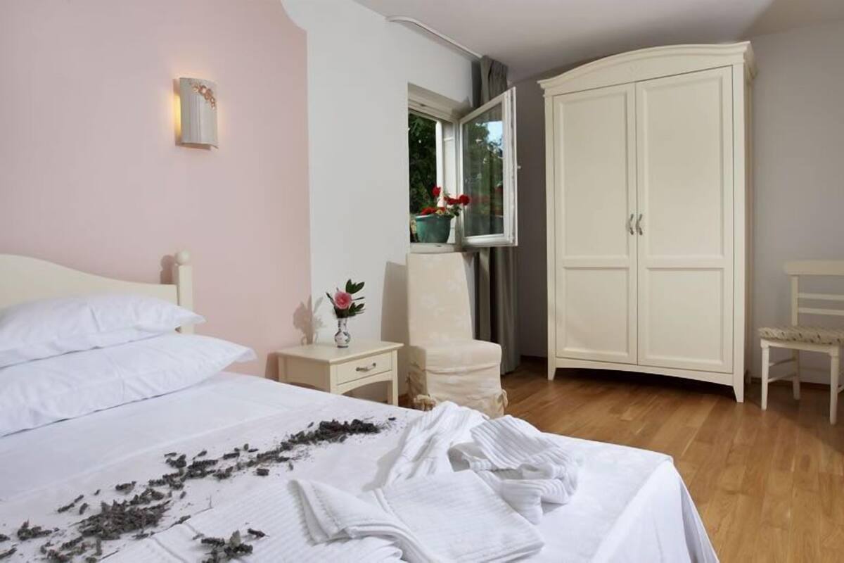 A bedroom with a bed, a nightstand, a chair, a wardrobe, and a window with a view of greenery.