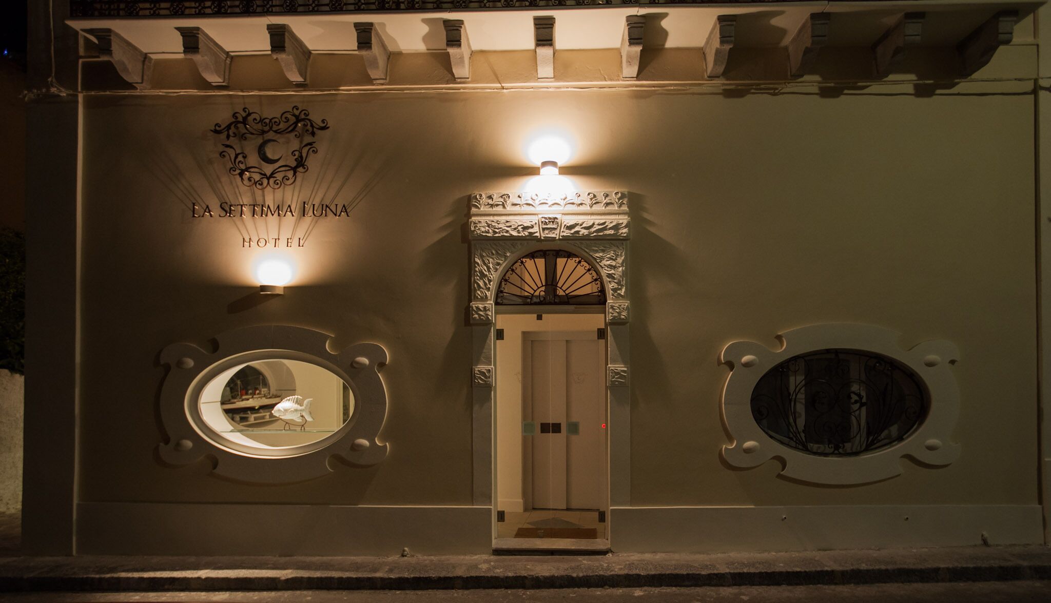 L’entrée de l’hôtel est dotée d’une porte centrale, de part et d’autre de laquelle se trouvent deux fenêtres rondes, chacune encadrée d’un décor. Au-dessus de la porte, on peut voir une enseigne indiquant le nom de l’hôtel et son logo.