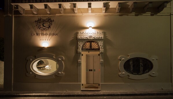 A hotel entrance with a central door flanked by two circular windows, each with a decorative frame. Above the door, there is a sign with the hotel's name and a logo. - La Settima Luna Hotel (Lipari)