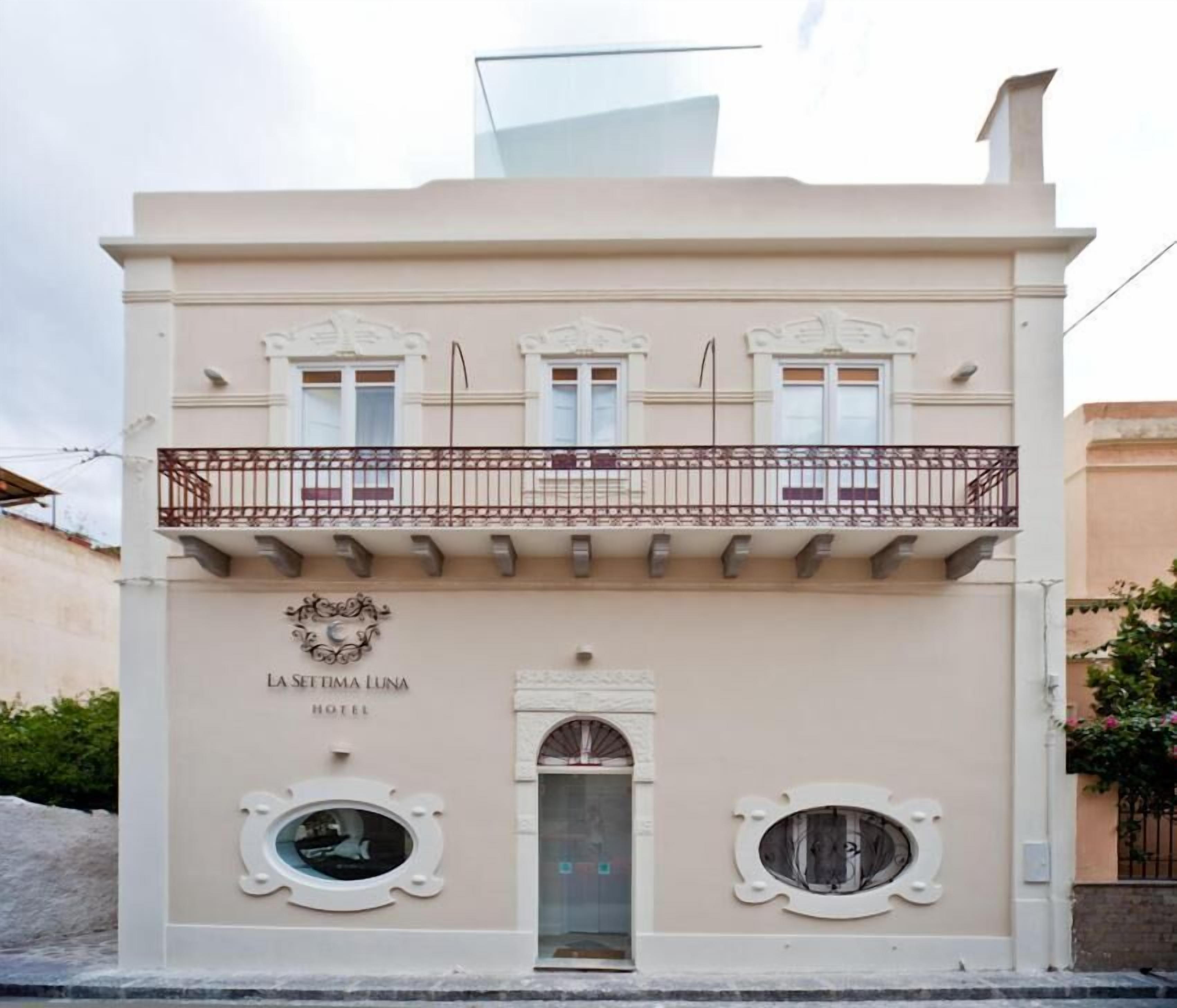 Un edificio con un balcón, un cartel que dice "LA SETTIMA LUNA HOTEL" y dos ventanas circulares debajo de la entrada.