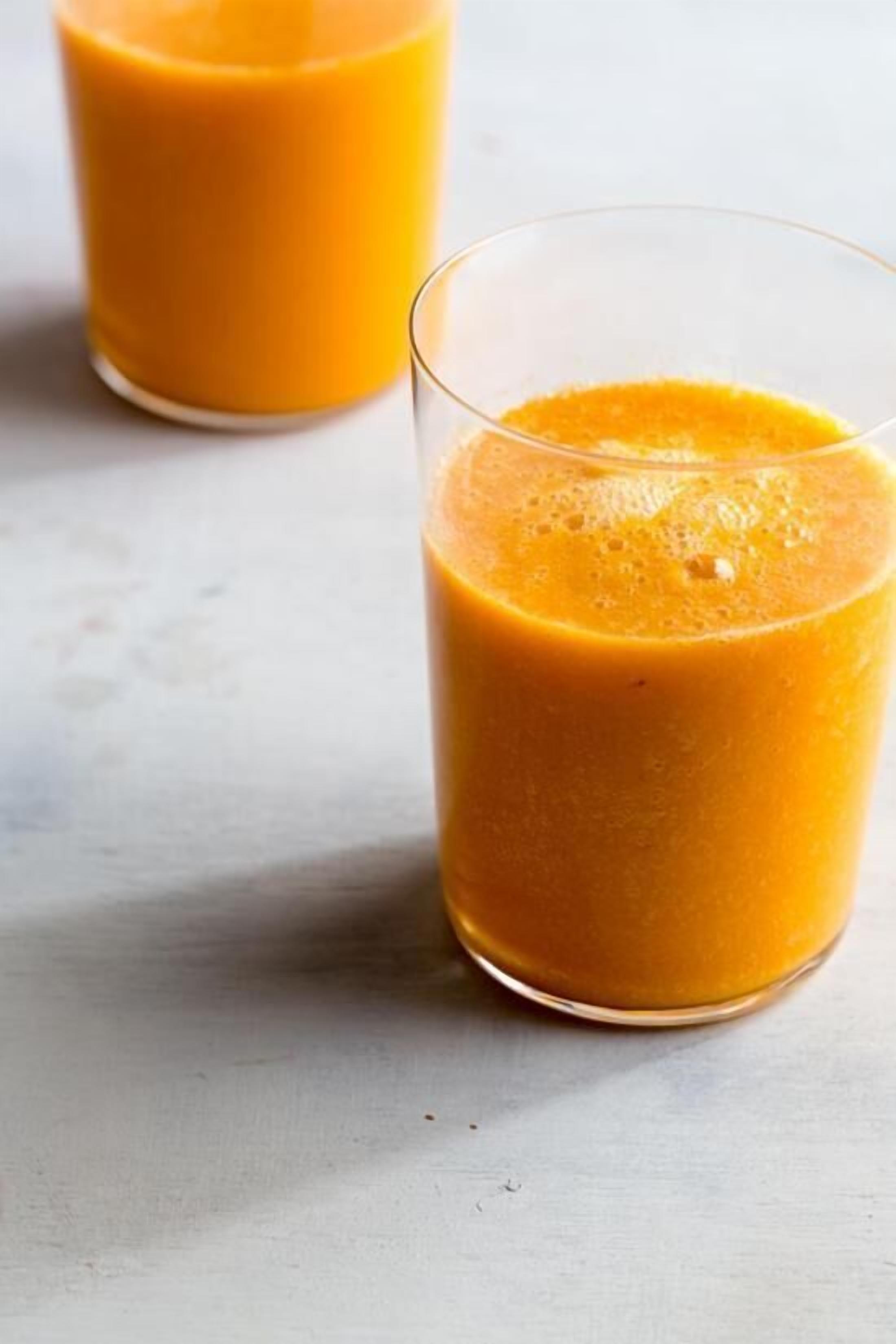 Dos vasos de jugo de naranja sobre una superficie blanca.
