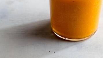 Dos vasos de jugo de naranja sobre una superficie blanca.