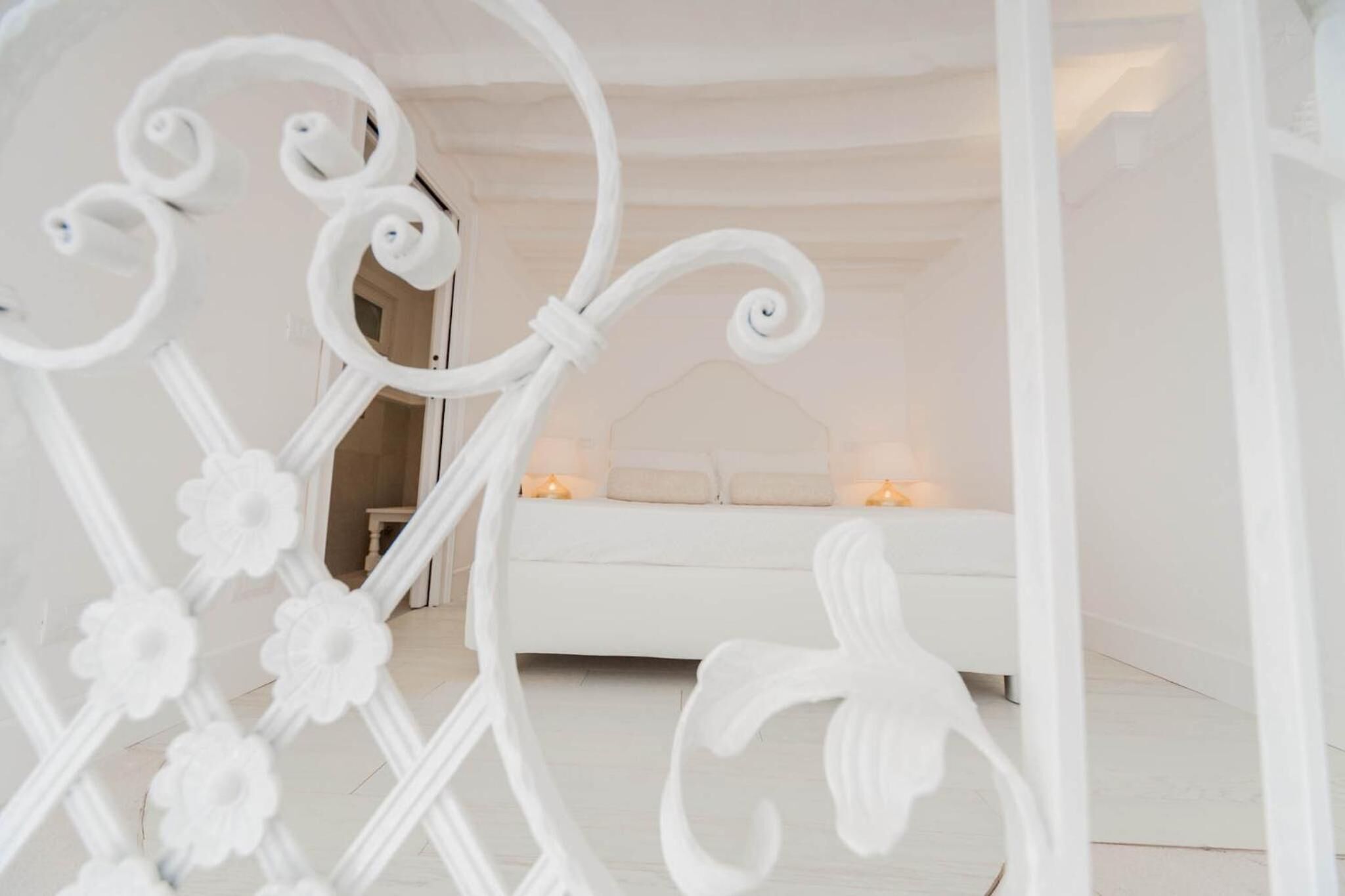 Une pièce blanche avec un lit, une petite table et une porte qui donne sur une autre pièce.