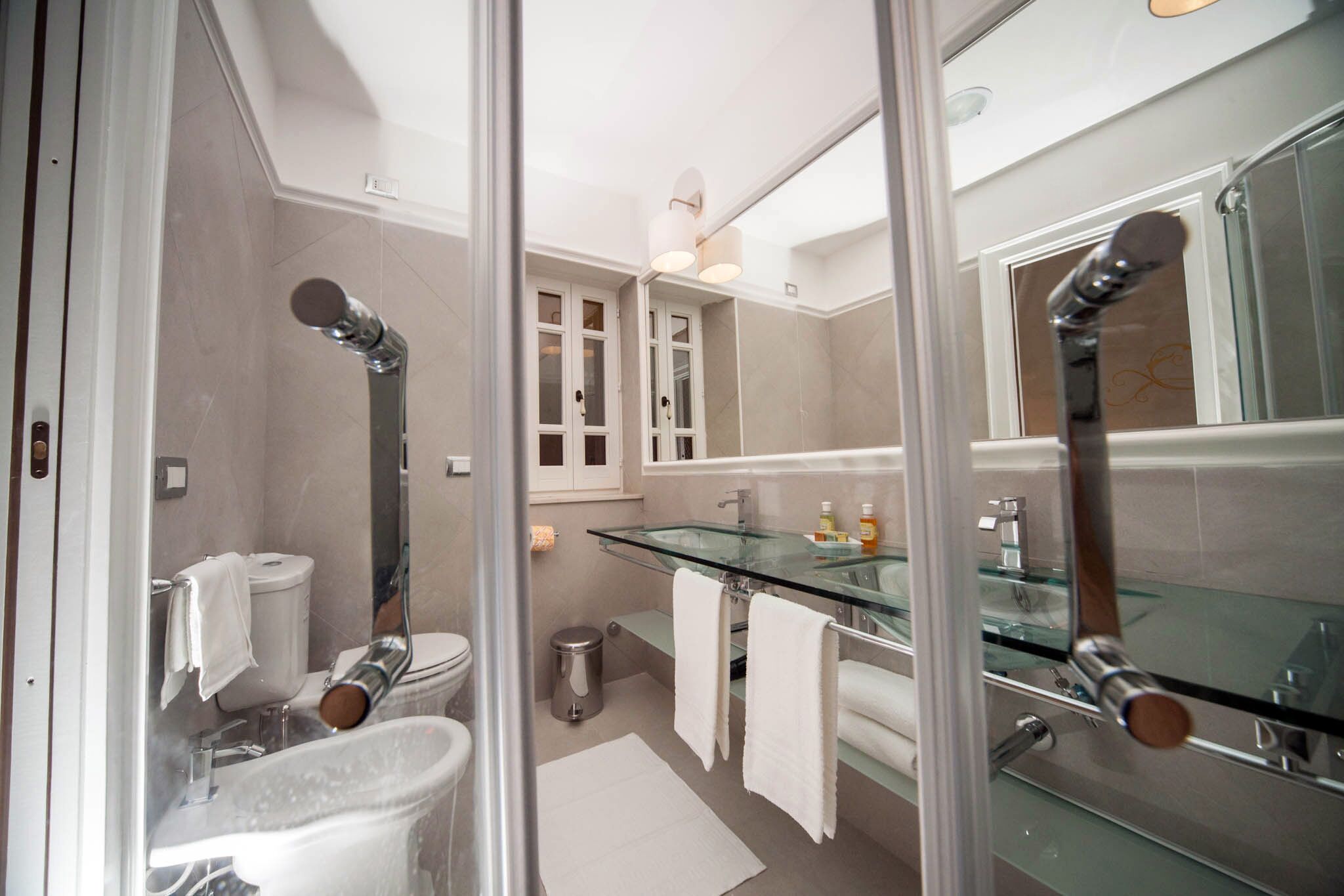 A modern bathroom with a glass shower enclosure, a glass sink, and a white toilet.