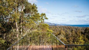 A wooden deck with glass railings overlooking a forested landscape with distant mountains.