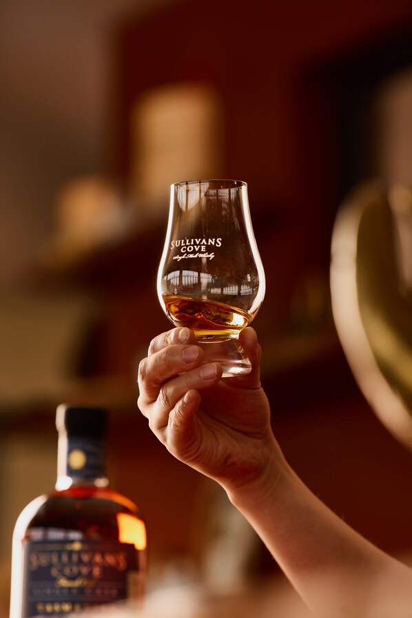 A hand holding a whiskey glass with a label reading "SULLIVANS COVE".
