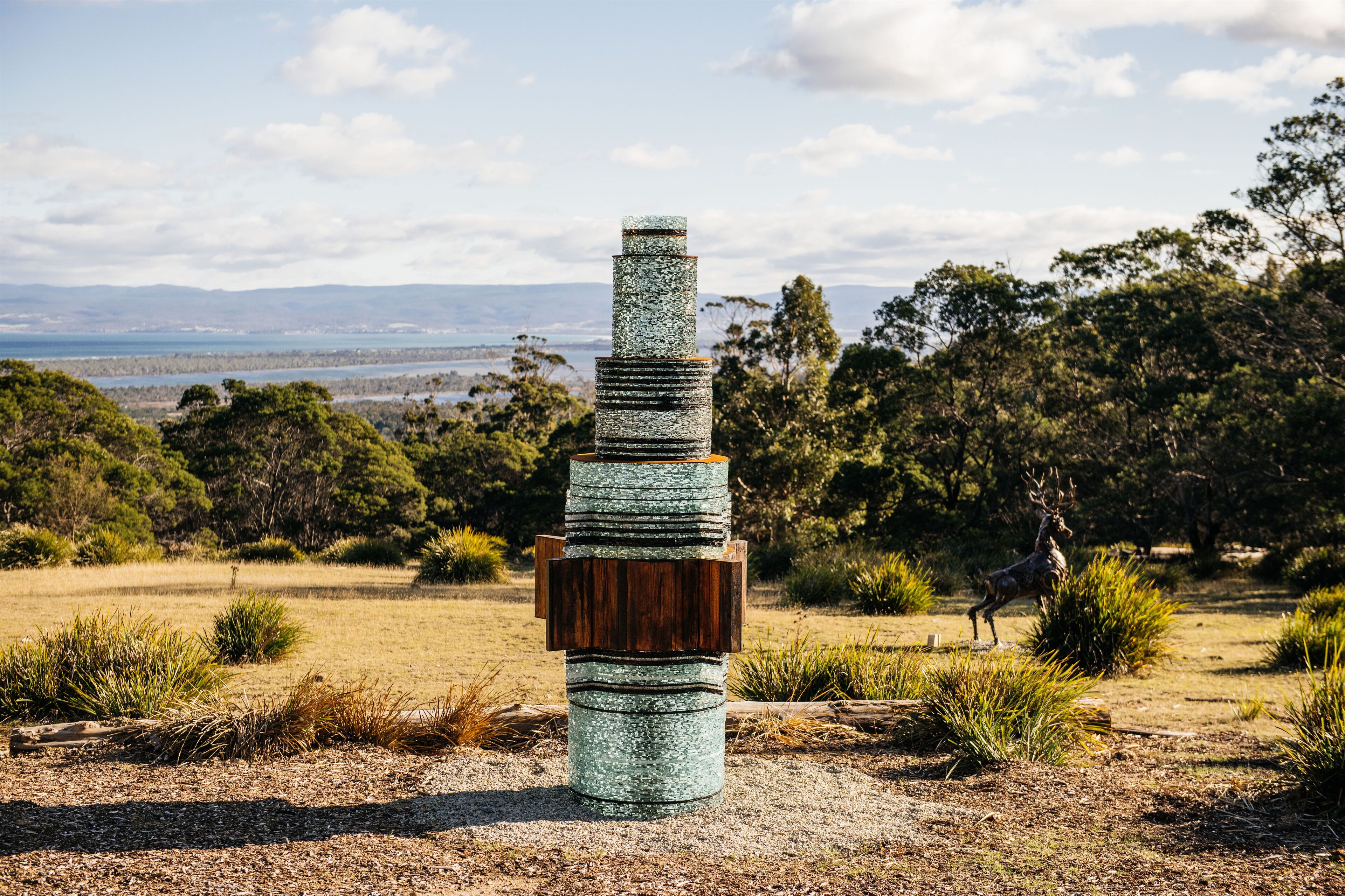 Una escultura en un entorno natural, con una vista distante de montañas y agua.