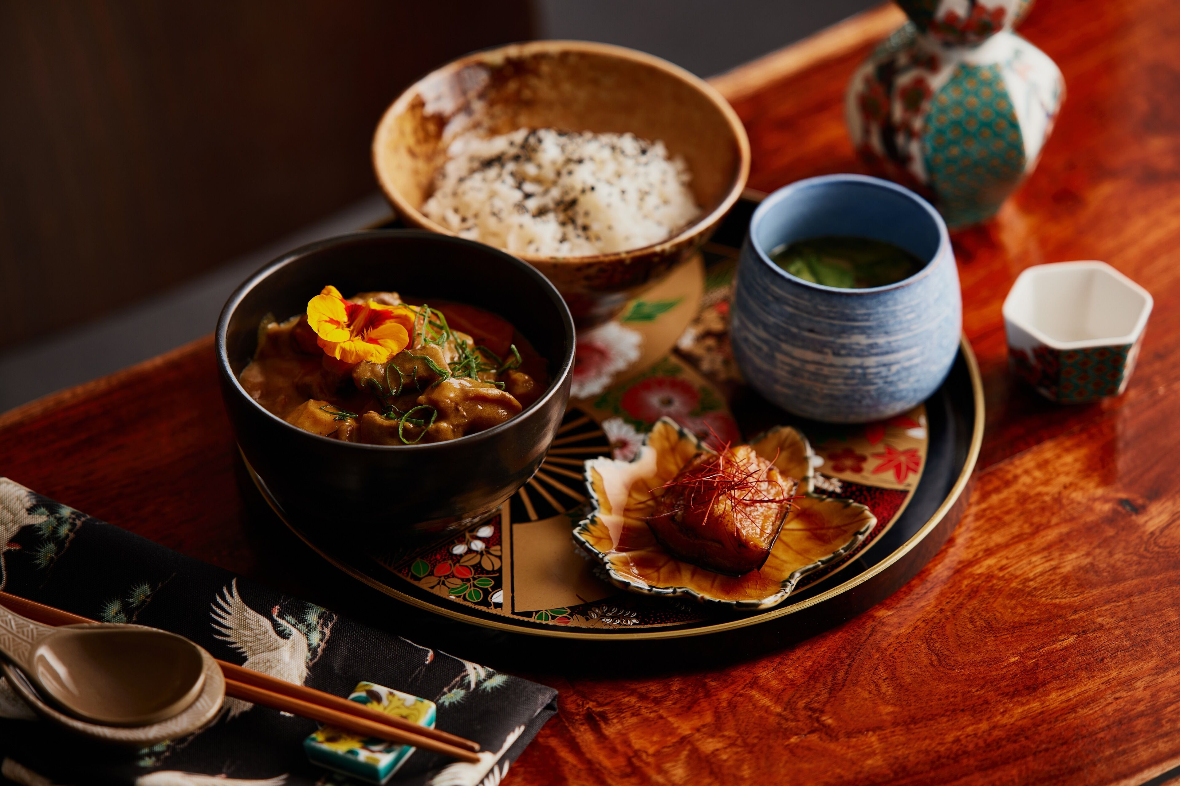 Un repas japonais traditionnel, composé d’un bol de soupe, d’une assiette de riz et d’un plat décoratif contenant du poisson.