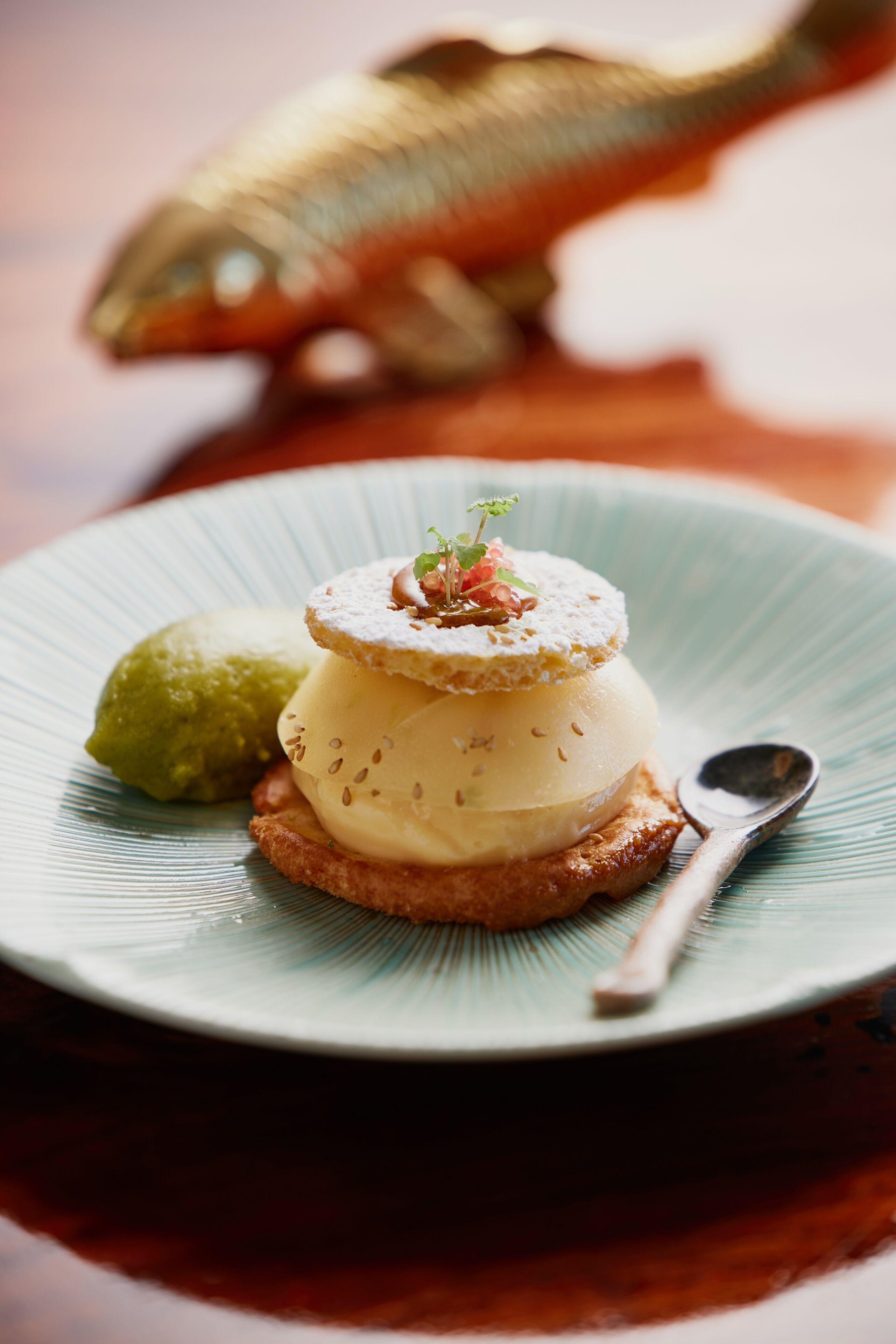 A dessert plate with a layered dessert, a green scoop, and a spoon.