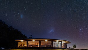 A modern, circular building with large windows, situated on a grassy field under a starry night sky.