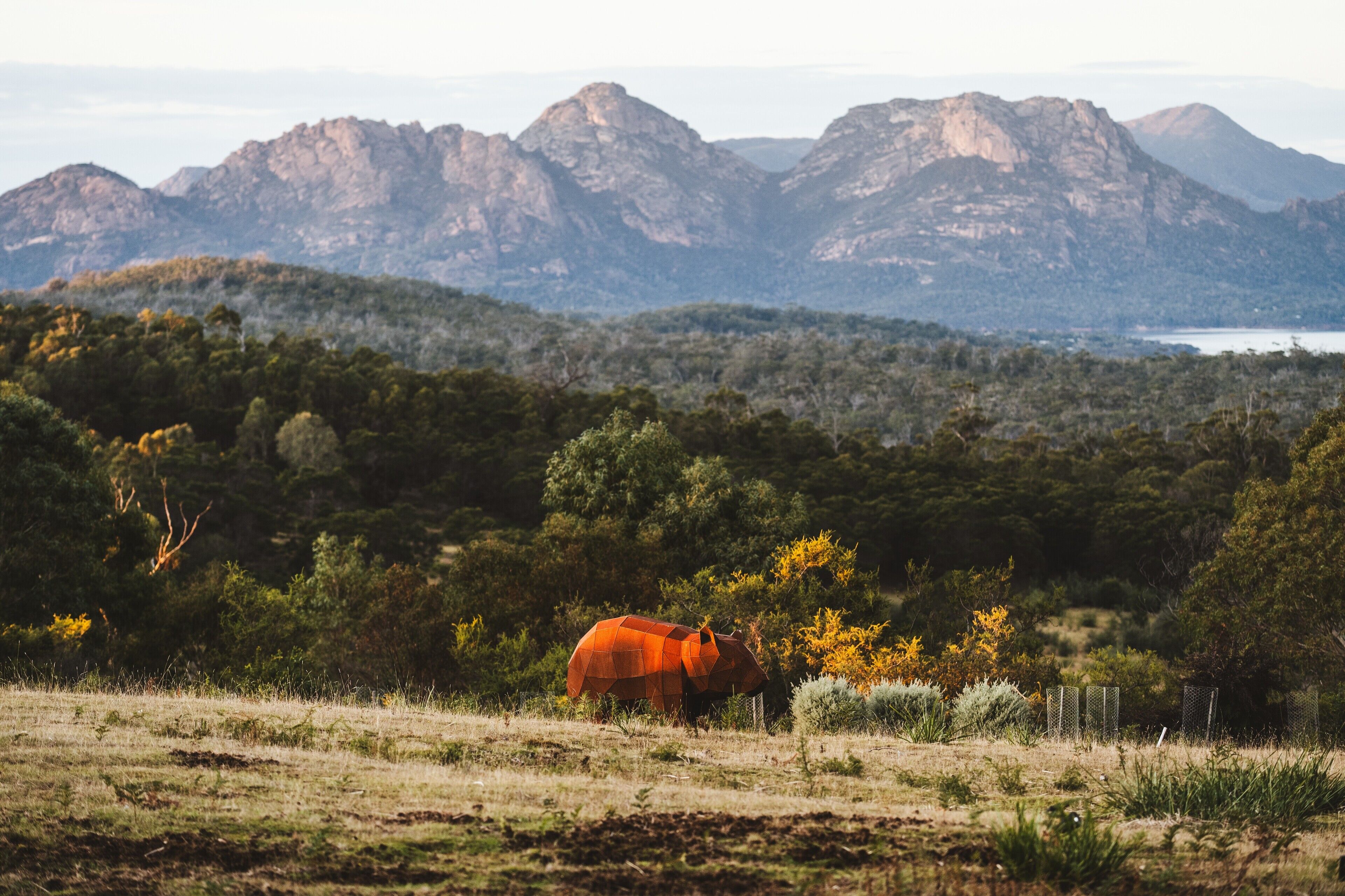 A landscape with a large, orange, geometric structure in the foreground, surrounded by greenery and mountains in the background.